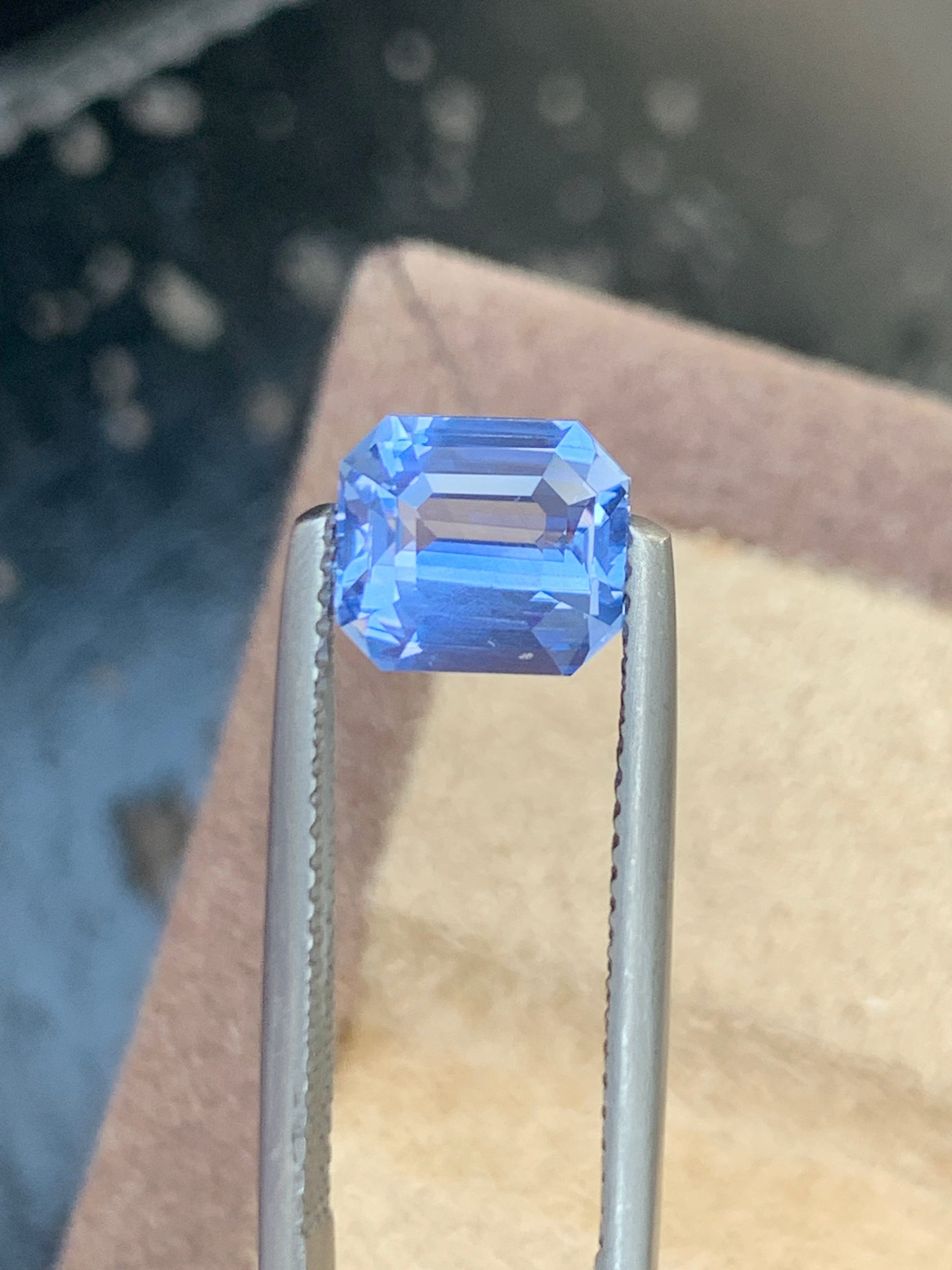 Un gros plan du Saphir Bleu rectangulaire facetté de 2,54 carats de Bonnot Paris maintenu par une pince métallique sur un fond flou met en valeur l'attrait de cette pierre précieuse.