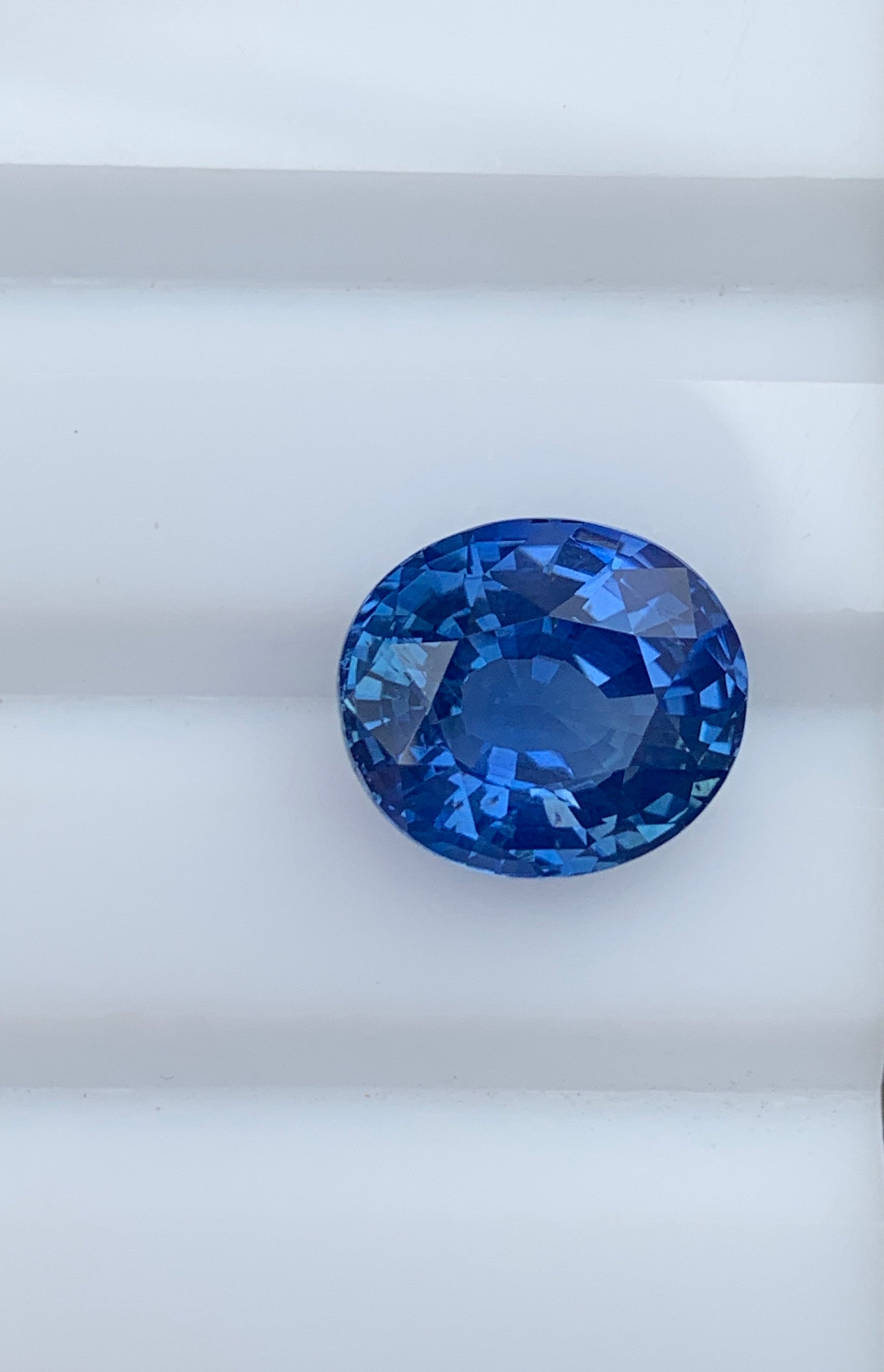 Un gros plan de la pierre précieuse Saphir Bleu 7,53ct de Bonnot Paris sur une surface blanche met en valeur sa surface facettée et brillante.