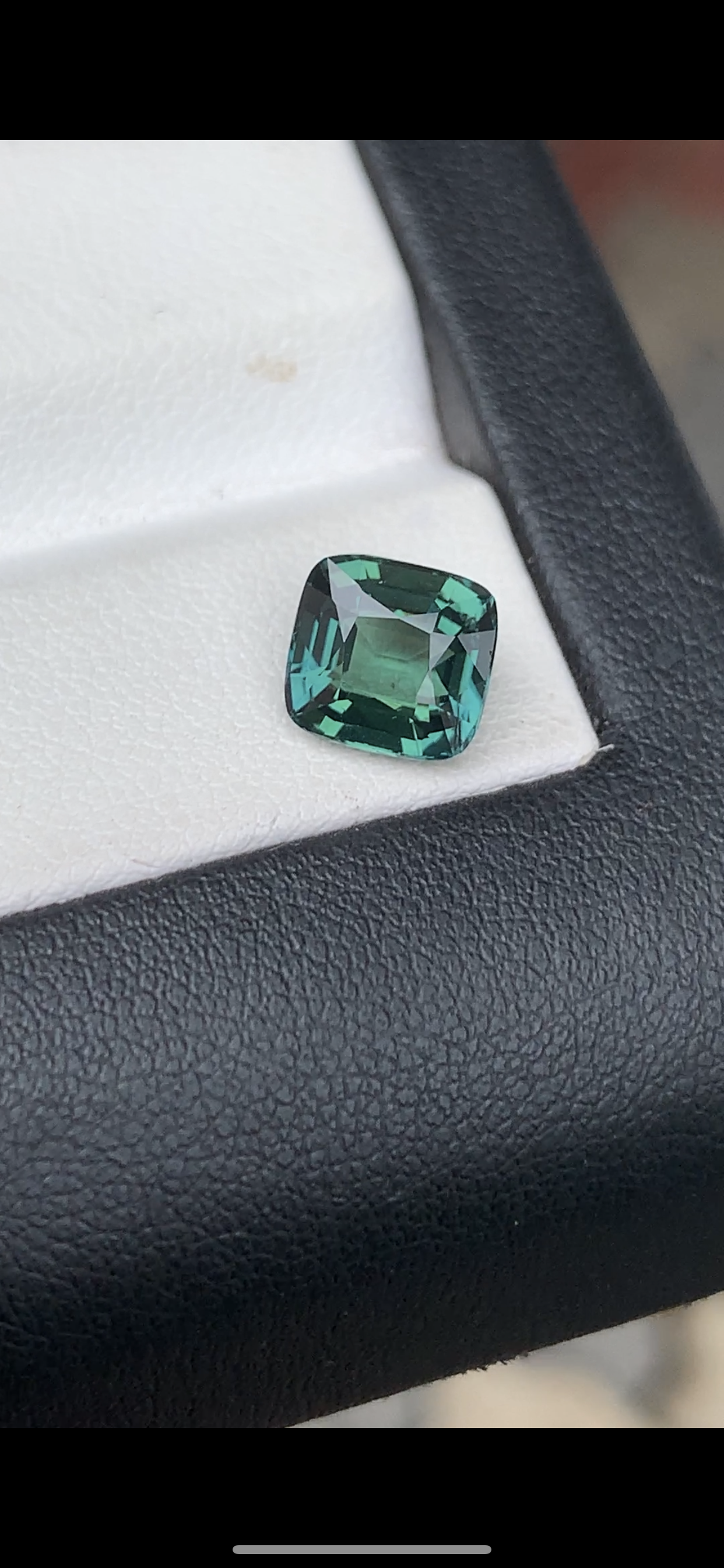 Le Saphir Teal de Bonnot Paris, une pierre précieuse captivante taille coussin de 2,55 carats, brille de nuances de vert sur une surface texturée blanche et noire.