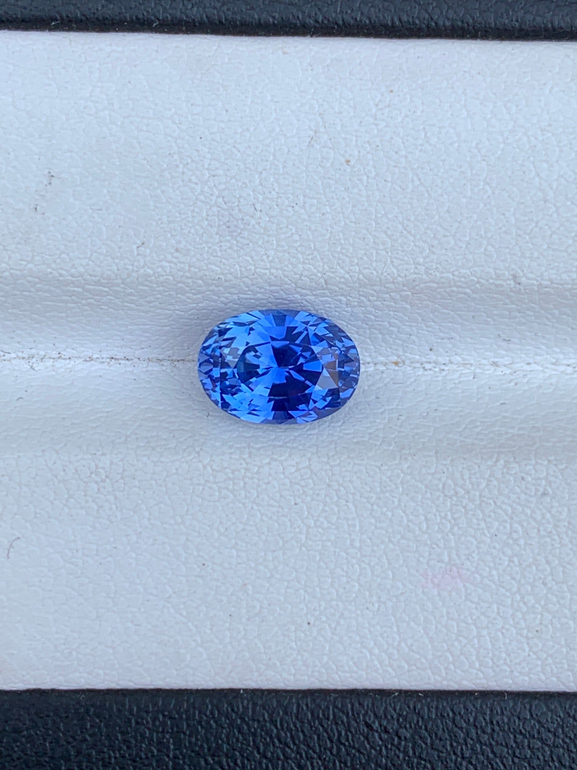 Une pierre précieuse Saphir Bleu vibrante de taille ovale • 3,02 ct de Bonnot Paris repose élégamment sur une surface blanche texturée, capturant la lumière et affichant une gamme étincelante de nuances bleues.