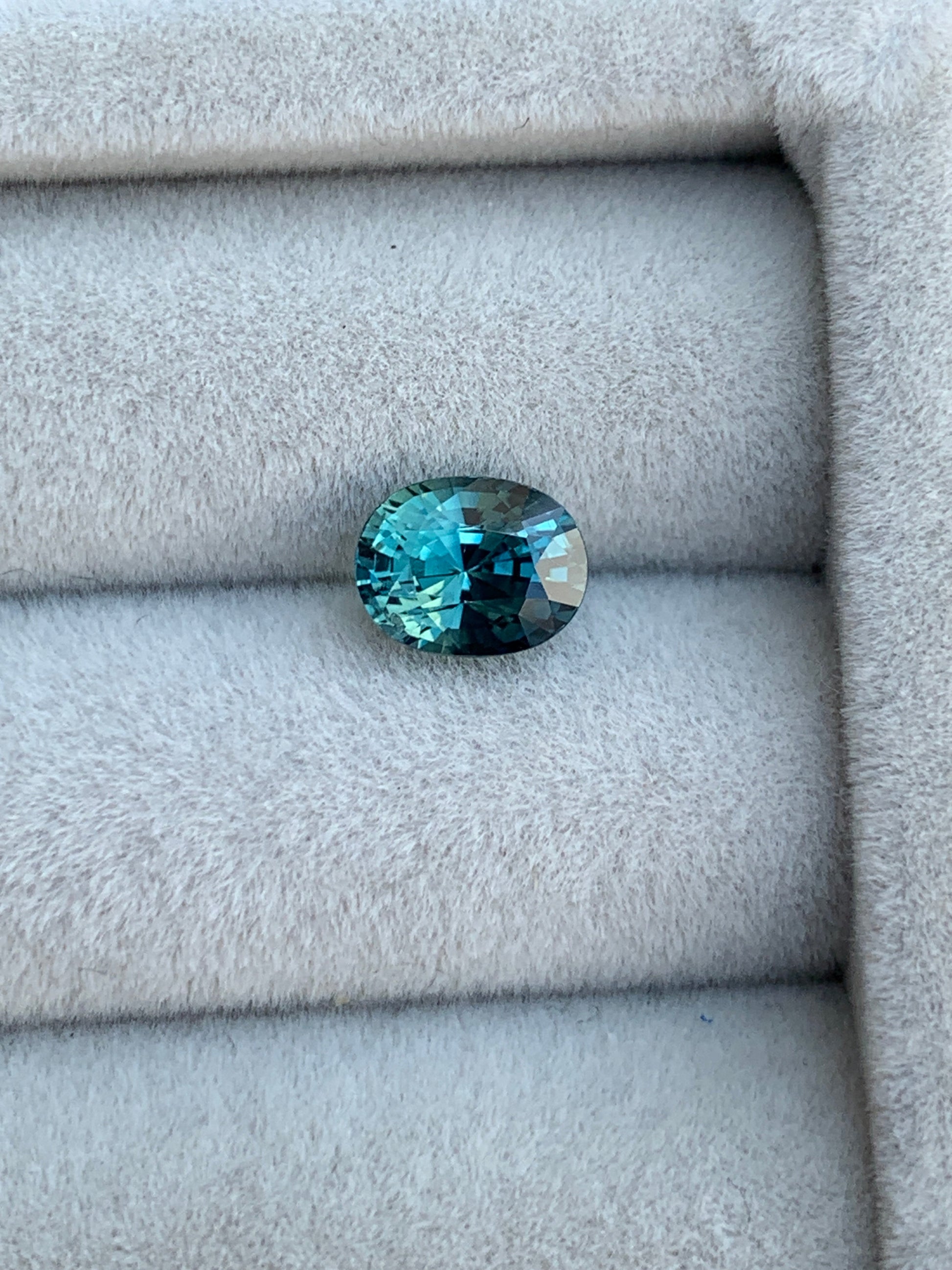 Le Saphir Teal 1,6ct de Bonnot Paris, avec son saphir de Madagascar étincelant de taille ovale, orne un doux fond de velours gris clair.