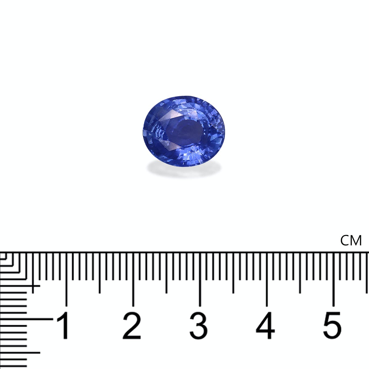 Une petite pierre précieuse Saphir Bleu de forme ovale de Bonnot Paris, scintillante de facettes bleu clair et bleu foncé, est centrée au-dessus d'une règle marquée en centimètres, indiquant qu'elle mesure environ 1 centimètre de large.