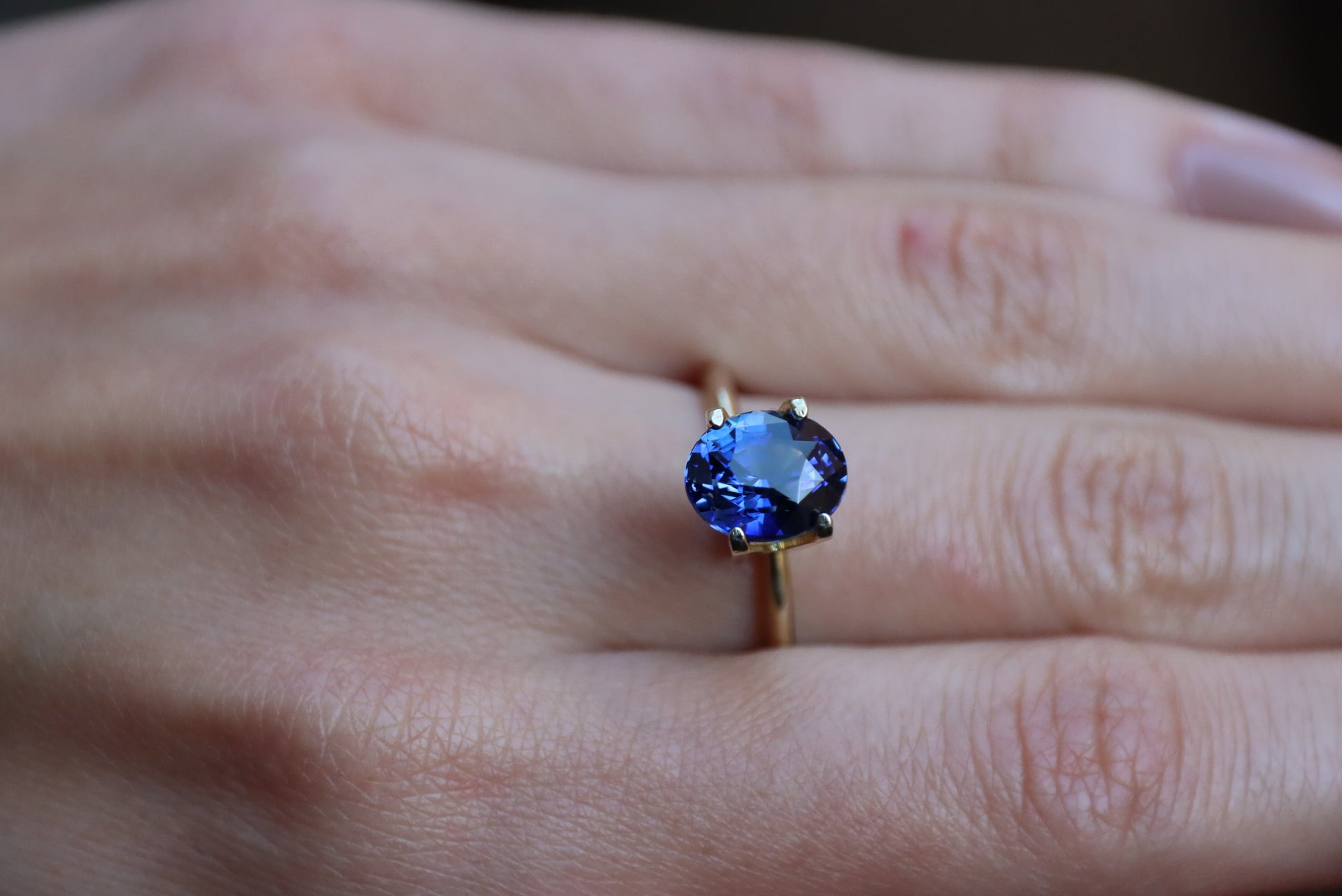 Gros plan d'une main portant au majeur la bague en or Saphir Bleu · 3,52 carats de Bonnot Paris, ornée d'une grosse pierre bleue ovale. La peau révèle sa couleur et sa texture naturelles.