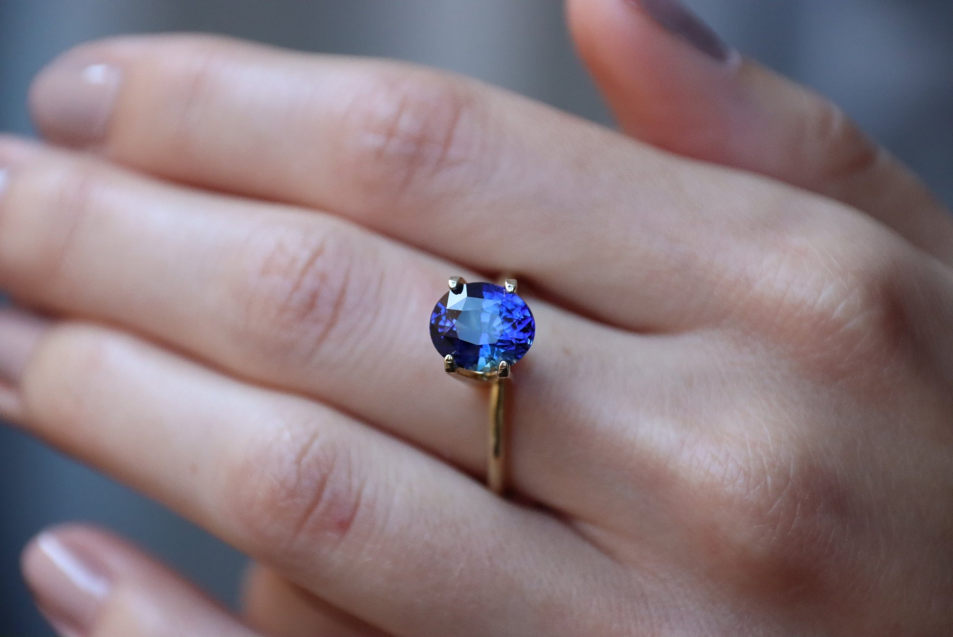 Un gros plan présente une main avec une manucure neutre polie portant la bague Bonnot Paris Saphir Bleu · 3,52 ct, comportant une pierre précieuse bleu foncé de taille ovale dans un cadre élégant, mettant en valeur sa couleur vibrante.