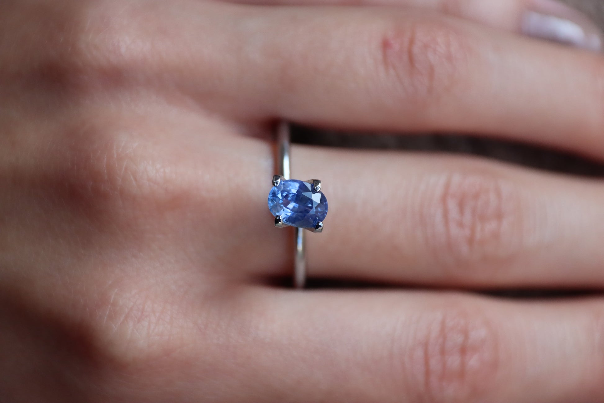 Un gros plan met en valeur une main ornée du Saphir Bleu de Bonnot Paris, une bague en argent ornée d'une pierre bleue ovale de 1,28 carat. La main repose sur une surface douce et texturée, mettant en valeur la couleur vibrante et l'éclat de la pierre.