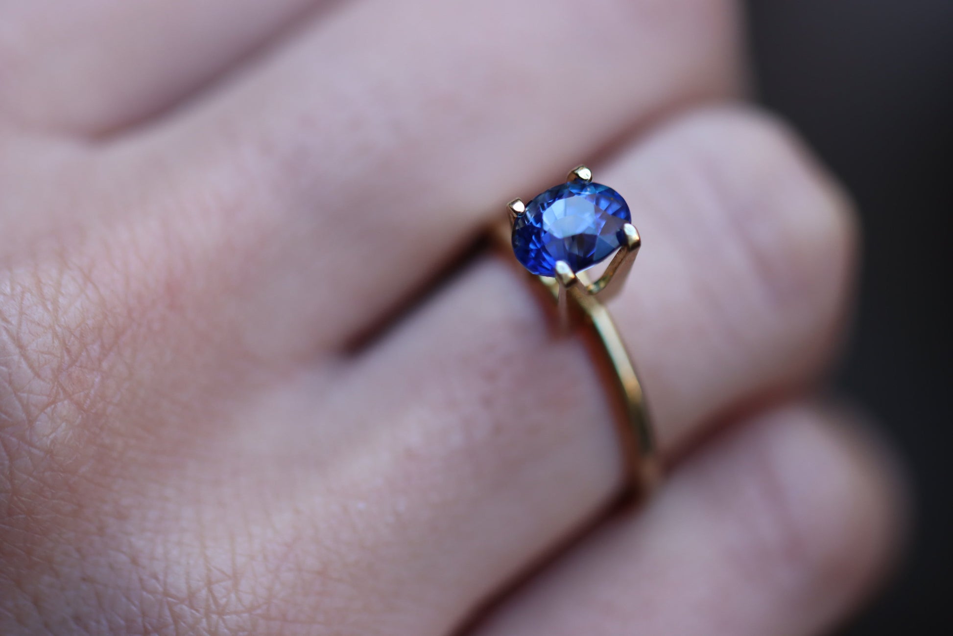 Gros plan d'une main portant la bague Saphir Bleu · 2,12 carats de Bonnot Paris, ornée d'une pierre bleue ronde sertie à griffes classique. L'arrière-plan flou met en valeur les détails de la bague.
