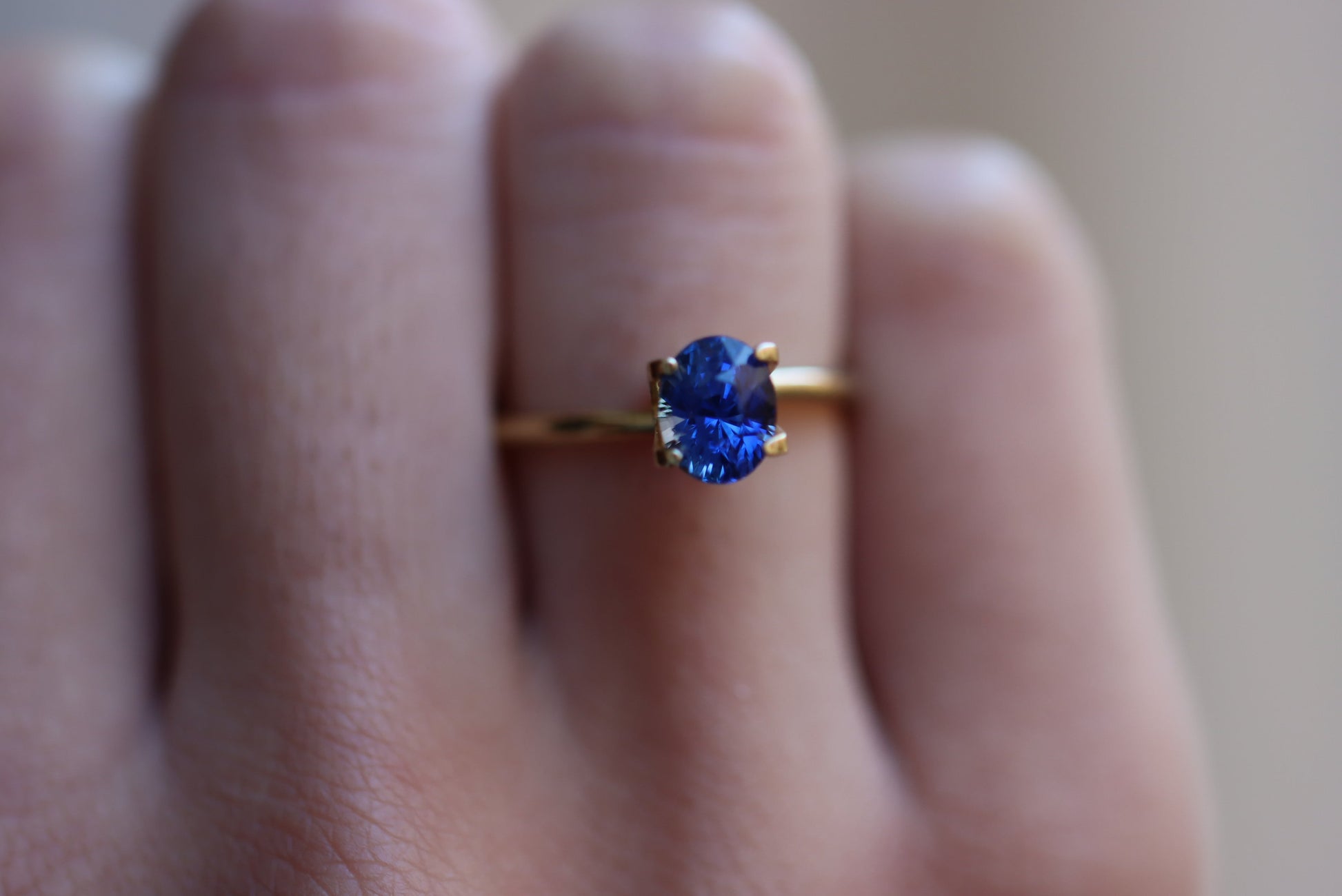 Une main met en valeur la bague Saphir Bleu · 2,12ct de Bonnot Paris, ornée d'une pierre précieuse bleue ovale sur un fond flou, soulignant son élégance.