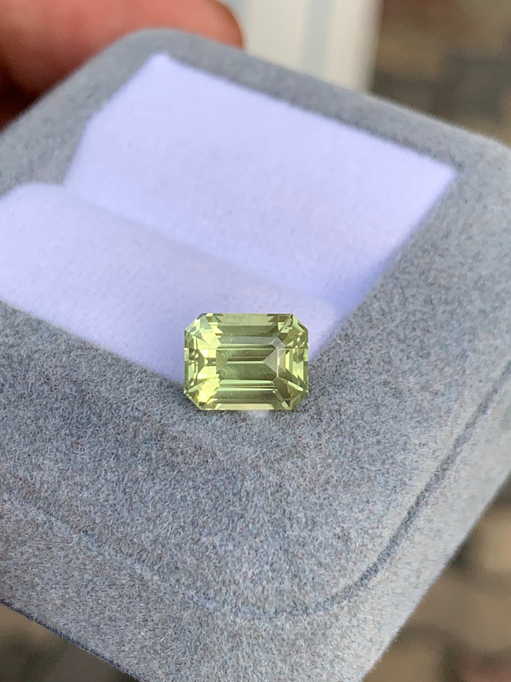 Le Saphir Jaune · 3,55 carats de Bonnot Paris est élégamment présenté dans un écrin gris ouvert doublé de blanc. Sa teinte vert pâle et ses facettes complexes captivent le regard, évoquant l'exotisme de Madagascar.