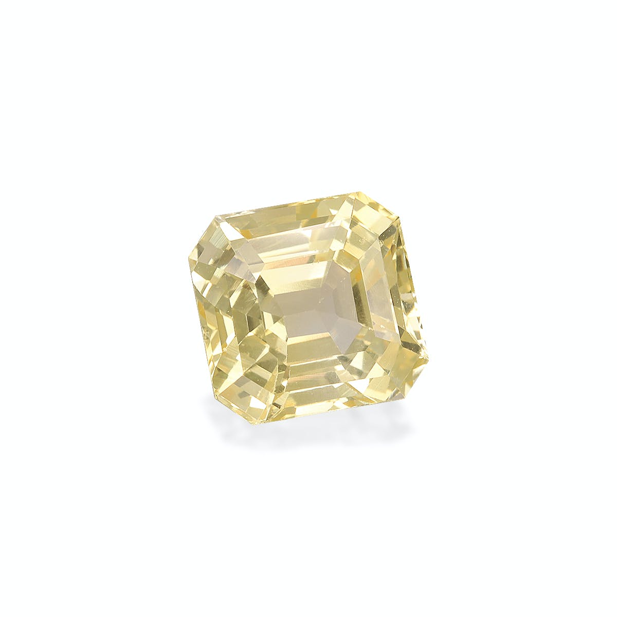 Le Saphir Jaune · 3,48 carats de Bonnot Paris est une pierre précieuse jaune scintillante, de taille rectangulaire, aux bords biseautés, sur un fond gris clair. Ses facettes captent la lumière, créant des reflets et un éclat vibrant.