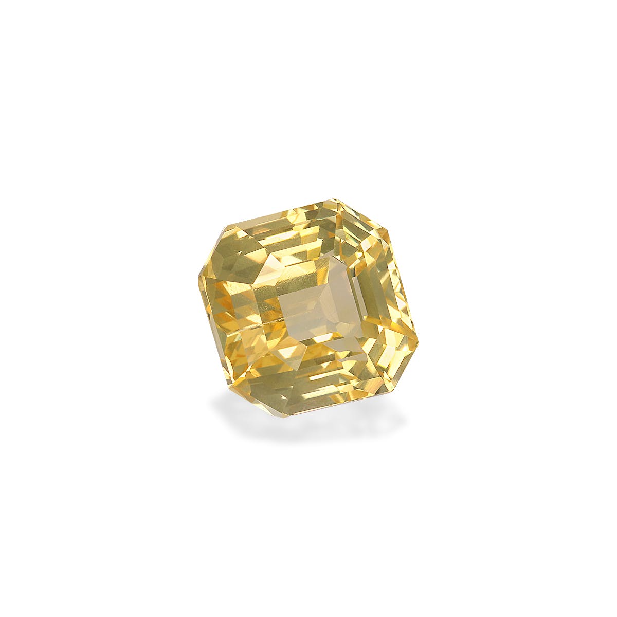 Le Saphir Jaune · 3,65ct de Bonnot Paris est une pierre précieuse taille émeraude jaune aux multiples facettes reflétant la lumière, positionnée sur un fond blanc et légèrement inclinée pour mettre en valeur sa forme géométrique et sa clarté.