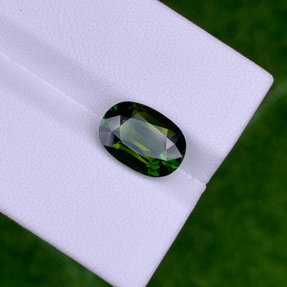 La Tourmaline Chrome · 3,04ct de Bonnot Paris est une pierre précieuse verte taille émeraude avec un bord sombre, présentée sur une surface blanche avec un fond vert flou.