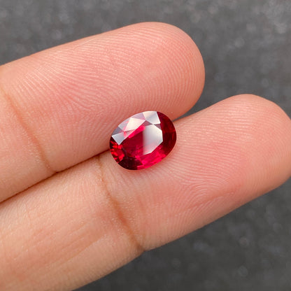 Les doigts tiennent un Rubis du Mozambique de 2,59 carats de Bonnot Paris, mettant en valeur sa pierre précieuse ovale facettée rouge foncé sur un fond sombre flou.