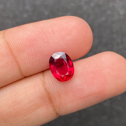 Gros plan d'une main tenant le Rubis du Mozambique de Bonnot Paris, une pierre précieuse ovale facettée rouge de 2,59 carats. Un fond gris foncé flou met en valeur la couleur vibrante de la pierre.
