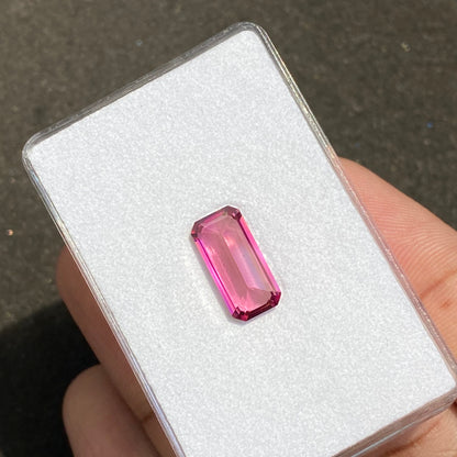 Une Tourmaline Rose de 3,95 carats de Bonnot Paris, vibrante et claire, est présentée alors que les doigts la tiennent contre une carte blanche, mettant en valeur sa pierre précieuse rose rectangulaire facettée qui reflète magnifiquement la lumière.