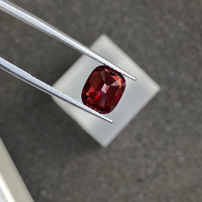 Une paire de pinces tient une pierre précieuse Spinelle Rouge rectangulaire facettée de 2,3 ct de couleur rouge foncé de Bonnot Paris au-dessus d'un arrière-plan flou.