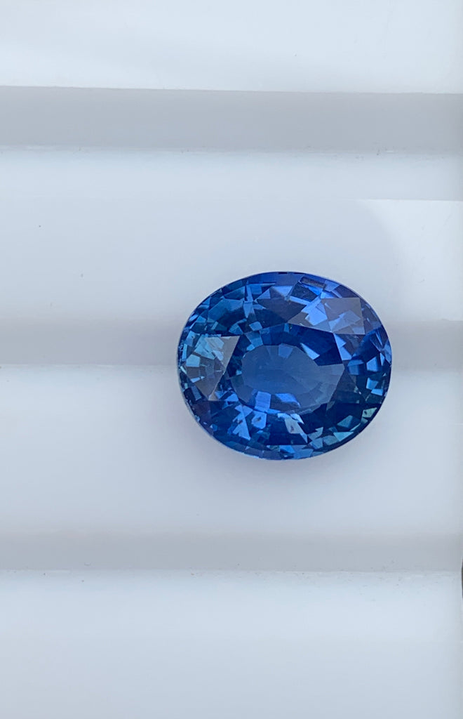 Un gros plan de la pierre précieuse Saphir Bleu 7,53ct de Bonnot Paris sur une surface blanche met en valeur sa surface facettée et brillante.