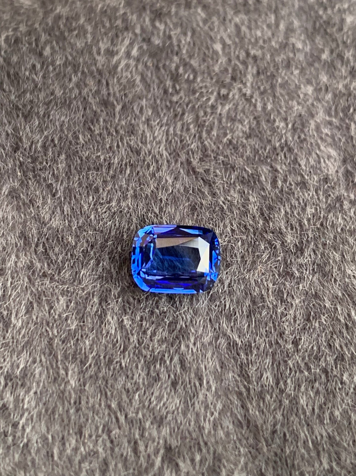 Le Saphir Bleu • 1,57ct de Bonnot Paris repose élégamment sur un tissu gris texturé, faisant écho à l'attrait exotique d'une pierre précieuse sri-lankaise avec ses surfaces facettées.