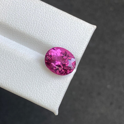 Une tourmaline rubellite ovale éclatante (4,35 carats) de Bonnot Paris repose sur une surface blanche texturée sur un fond sombre et flou. Ses facettes complexes et sa riche teinte scintillent de mille feux.