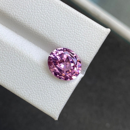Un spinelle rose de 3,93 carats de Bonnot Paris repose sur une surface blanche texturée en angle, avec un fond sombre flou qui accentue sa couleur vibrante et ses facettes complexes.