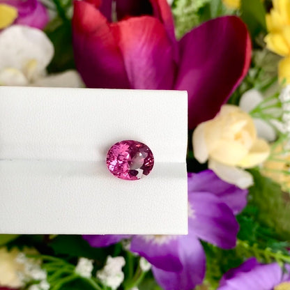 La Tourmaline Rubellite de Bonnot Paris, pèse 4,35 ct et est élégamment présentée sur une surface blanche avec des fleurs rouges et violettes en arrière-plan.