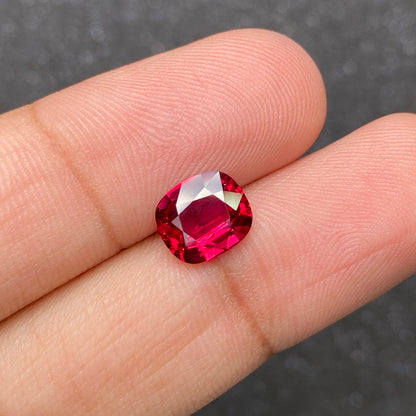 Un gros plan montre une main tenant la pierre précieuse Rubis du Mozambique de 2,57 ct de Bonnot Paris sur un fond sombre, sa surface rouge rosé facettée scintillant de couleurs et de clarté vibrantes.