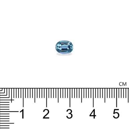 Une petite gemme bleue ovale de Bonnot Paris, ressemblant à une Aigue-Marine de 1,08 ct aux reflets célestes, repose sur une surface blanche. Sous la pierre précieuse se trouve une règle en centimètres, indiquant sa longueur d'environ 0,8 cm.