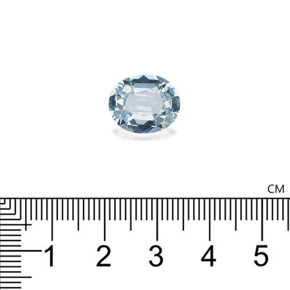 Une petite Aigue-Marine ovale de 5,23 carats de Bonnot Paris repose gracieusement sur une surface blanche, sous laquelle est posée une règle. La règle, graduée en centimètres, indique les dimensions de la pierre : environ 1,5 cm de long, dans son ravissant ton bleu clair.