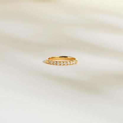 L'Alliance La Discrète de Bonnot Paris arbore une bague en or sertie de petits diamants naturels scintillants. Son design taille rond-brillant, d'une élégante simplicité, capte magnifiquement la lumière sur un fond clair et légèrement flou.