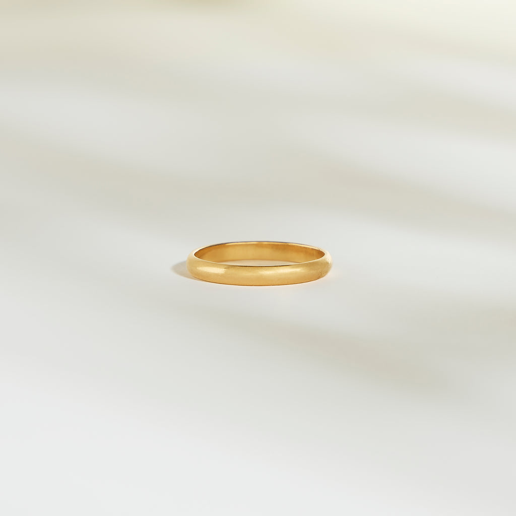 L'Alliance L'Authentique, un simple anneau en or signé Bonnot Paris, repose sur une surface pâle et légèrement éclairée. Les ombres subtiles qui l'entourent créent une atmosphère calme et élégante.