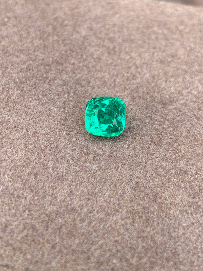 L'Émeraude taille coussin • 1,15ct de Bonnot Paris met en valeur sa teinte verte lumineuse sur une surface brune douce et texturée, reflétant magnifiquement la lumière de ses facettes.