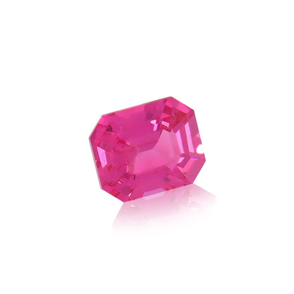 Un Spinelle Mahenge rose vibrant • 2,15 ct de Nascendi Paris, doté d'une taille émeraude à multiples facettes qui reflètent la lumière, repose sur une surface blanche brillante, projetant un petit reflet et incarnant l'élégance des bijoux sur mesure.