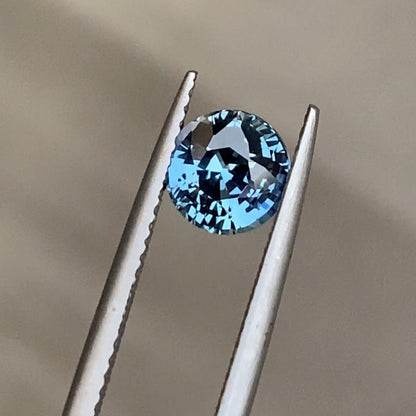 Gros plan sur le Saphir Teal de Bonnot Paris, une pierre précieuse de 1,55 carat, maintenue par une pince en argent sur un fond neutre. Il scintille de mille feux grâce à ses multiples facettes, soulignant sa clarté et sa couleur turquoise éclatante.