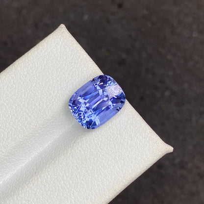 Une photo en gros plan présente le Saphir Bleu · 5,19 ct de Bonnot Paris, une pierre précieuse bleu vif taille coussin avec une surface facettée qui reflète brillamment la lumière, reposant sur une surface blanche texturée sur un fond sombre.