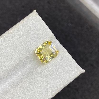 Le Saphir Jaune · 3,03 ct de Bonnot Paris, un diamant jaune taille radiant présenté sur un support blanc sur un fond sombre, met en valeur l'éclat et la clarté de la pierre précieuse.