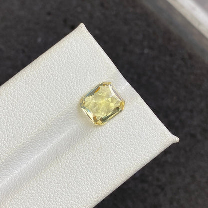 Le Saphir Jaune · 3,03ct de Bonnot Paris, une pierre précieuse jaune taille carrée, est présenté sur une surface texturée blanche avec un fond sombre et flou.