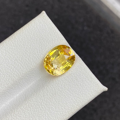 Une pierre précieuse jaune ovale étincelante de 4,5 carats, Saphir Jaune de Bonnot Paris, est présentée sur une surface blanche sur un fond sombre.