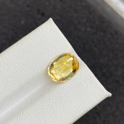Le Saphir Jaune · 4,5 ct de Bonnot Paris est une pierre précieuse jaune polie de taille ovale présentée sur une surface blanche sur un fond sombre, avec une qualité brillante et translucide qui reflète magnifiquement la lumière.