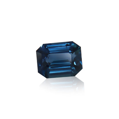 Le Saphir Teal · 2,57 ct de Bonnot Paris, une pierre précieuse taille émeraude provenant de Madagascar, présente des facettes nettes et des surfaces réfléchissantes sur un fond blanc, révélant de superbes nuances de bleu foncé et des touches de sarcelle.
