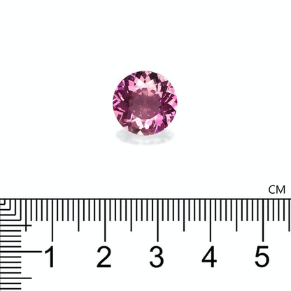 Une tourmaline cuprifère de 5,22 carats de Bonnot Paris est sertie sur une surface blanche, à côté d'une règle graduée en centimètres. Cette pierre rose ronde mesure environ 1,5 cm de diamètre et reflète magnifiquement la lumière avec un effet scintillant. La règle est placée horizontalement sous la pierre.