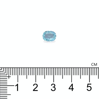 Une petite tourmaline paraïba ovale de Bonnot Paris est sertie sur un fond blanc. Sous la pierre bleue de 0,92 ct se trouve une règle graduée en centimètres, indiquant une longueur légèrement supérieure à 1 cm.