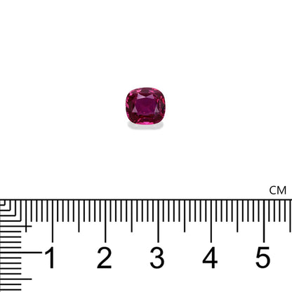 Le Saphir Rose · 2,55 ct de Bonnot Paris, une pierre précieuse rubis taille coussin rouge foncé, repose sur une surface blanche à côté d'une règle centimétrique, montrant sa surface polie et réfléchissante et sa taille inférieure à 1 cm.