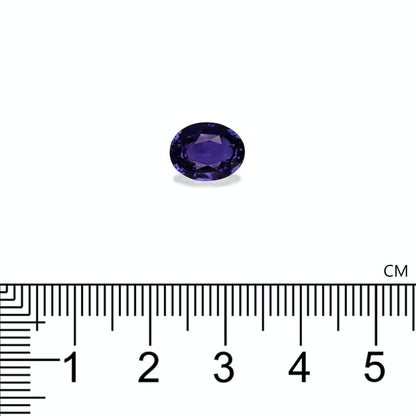 Une pierre précieuse Saphir Violet · 3,5 ct de Bonnot Paris, petite et de forme ovale avec une teinte violet foncé, est positionnée au-dessus d'une échelle centimétrique, indiquant qu'elle mesure environ 1 cm de large.