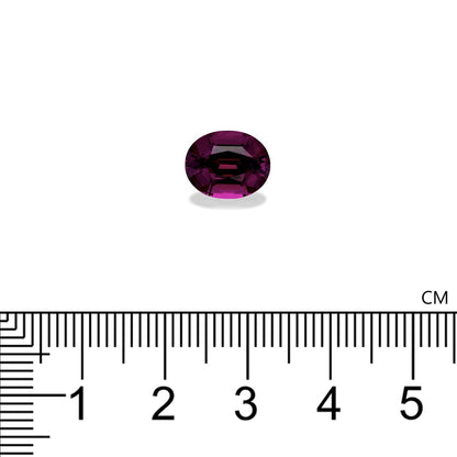 Sur une surface blanche repose une petite ombalite de grenat ovale, d'un violet profond. En dessous, une règle noire et blanche graduée de 0 à 5 cm indique la taille approximative de la pierre, soit 0,8 cm. Cette magnifique pièce de 4,06 carats est signée Bonnot Paris.