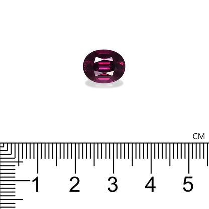 Une petite gemme violette de forme ovale présentée sur un fond blanc avec une règle centimétrique en dessous pour l'échelle, révélant que le Grenat Umbalite de Bonnot Paris mesure environ 1 cm de long et pèse 4,82 ct.