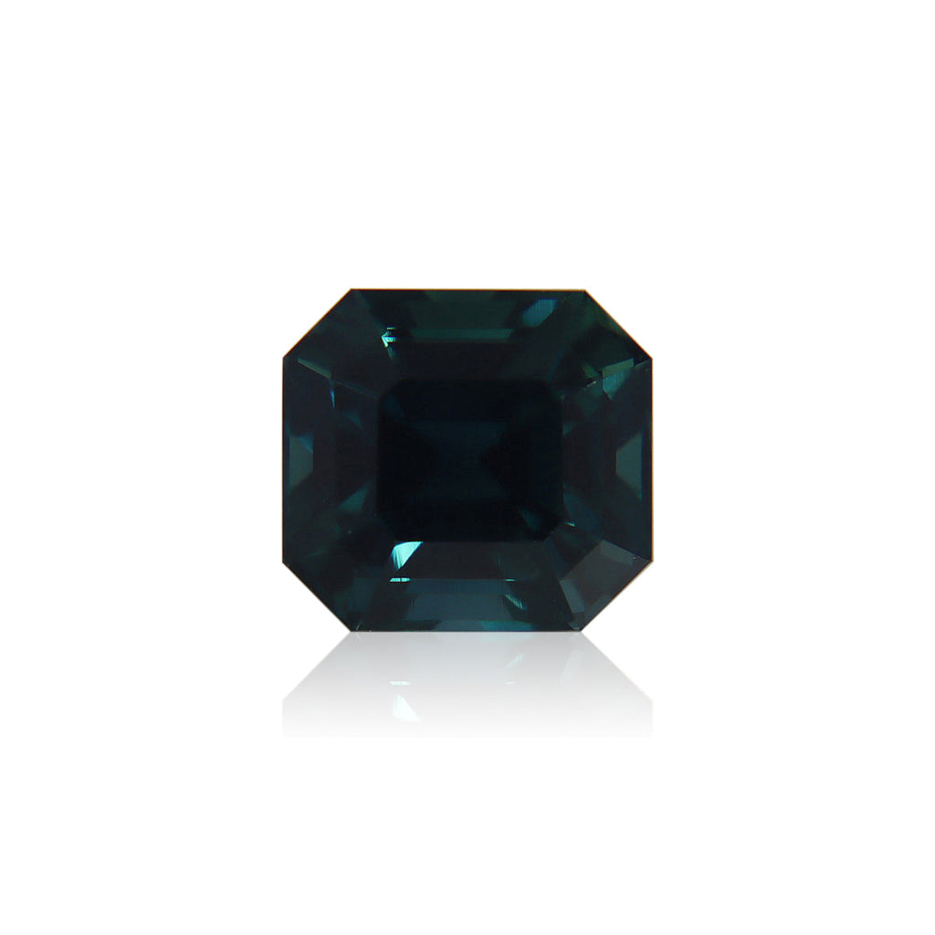 Le Saphir Teal de Bonnot Paris · 3,51 ct, une pierre précieuse rectangulaire bleu profond avec une taille émeraude et des bords biseautés, brille sur un fond blanc uni dans une forme symétrique reflétant une riche teinte bleue.