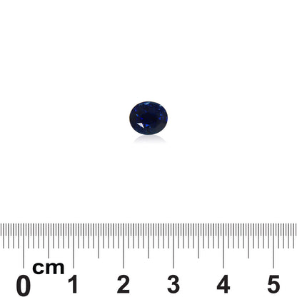 Une petite pierre précieuse ronde Saphir Bleu · 2,07 carats, d'un bleu profond, signée Bonnot Paris, est posée sur un fond blanc uni, une règle en dessous indiquant un diamètre d'environ 0,6 cm. La pierre présente une couleur bleue intense et une surface brillante.