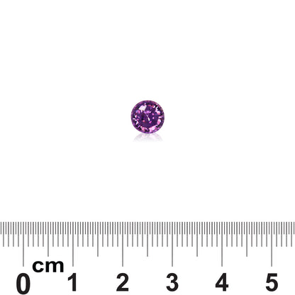 Une petite pierre précieuse ronde Saphir Violet de Bonnot Paris, pesant 1,38 carat, est placée au-dessus d'une règle graduée en centimètres pour en représenter la taille. Ses facettes scintillent magnifiquement en reflétant la lumière.