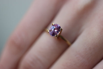Une personne porte la bague Bonnot Paris Saphir Violet en or 1,59 carat, ornée d'une pierre violette ovale fixée par quatre griffes. Le fond légèrement flou met en valeur le design complexe et la couleur vibrante de la bague.