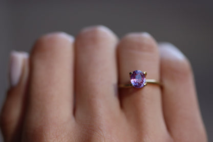 Une main met en valeur la bague en or Bonnot Paris « Saphir Violet · 1,51 ct » avec une pierre précieuse violette, sertie sur un fond légèrement flou qui met en valeur son design.