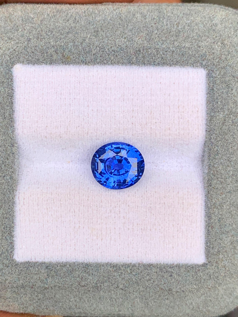 Un Saphir Bleu de 2,60 carats de Bonnot Paris, originaire du Sri Lanka, est présenté sur un fond blanc et gris, la lumière se reflétant sur ses facettes.
